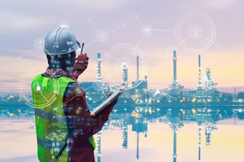 Lavoratore con dispositivi di sicurezza che parla al radio mentre osserva l'esterno di una fabbrica