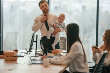 Uomo con suo figlio. Il bambino piccolo è in ufficio dove un gruppo di persone sta lavorando insieme.